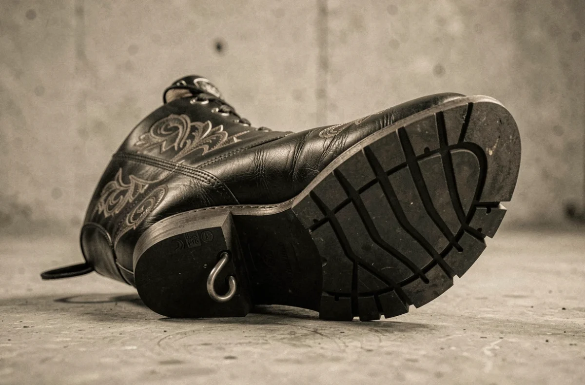 Gros plan d'une bottine cowboy noire pour moto montrant les détails de cuir repoussé, l'insert de protection cheville CE et la semelle antidérapante